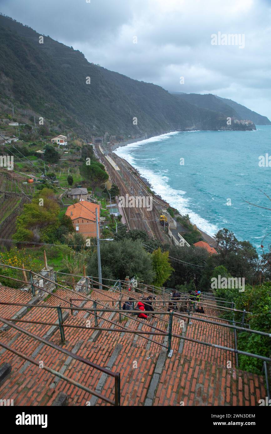 Cinque Terre, Italien – 03. Januar 2024: Touristen klettern die Treppen vom Bahnhof nach Riomaggiore mit Berg- und Meeresküste hinauf Stockfoto