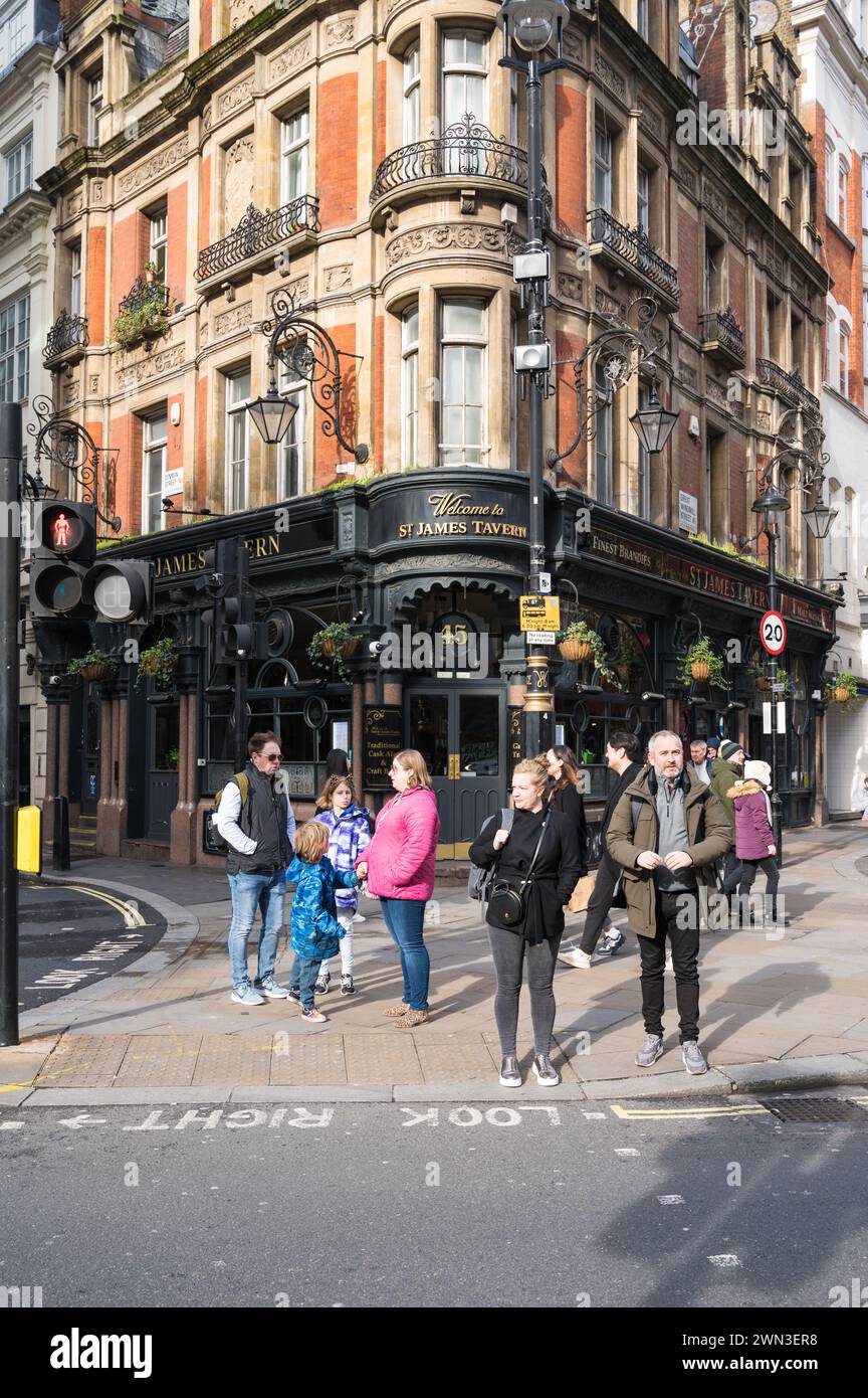 Leute, die in Soho vor der St. James Tavern spazieren gehen, einem traditionellen Pub an der Ecke Great Windmill Street und Denman Street Soho London UK Stockfoto