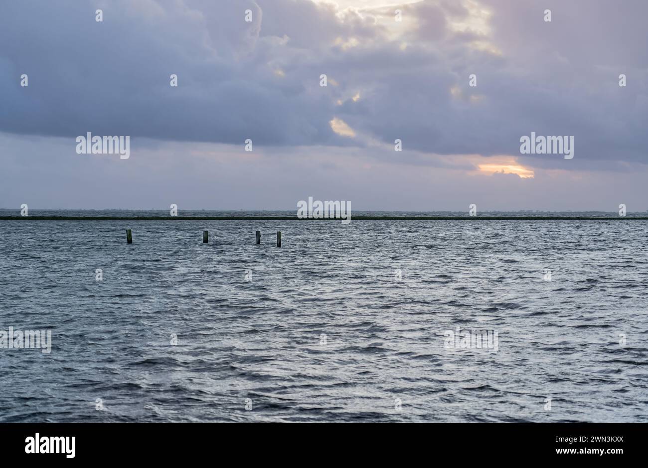 Das ruhige Wasser des überfluteten Überlaufgebietes reflektiert Pastelltöne des Abendhimmels, Deich grenzt an den See in ruhiger und malerischer niederländischer Landschaft Stockfoto