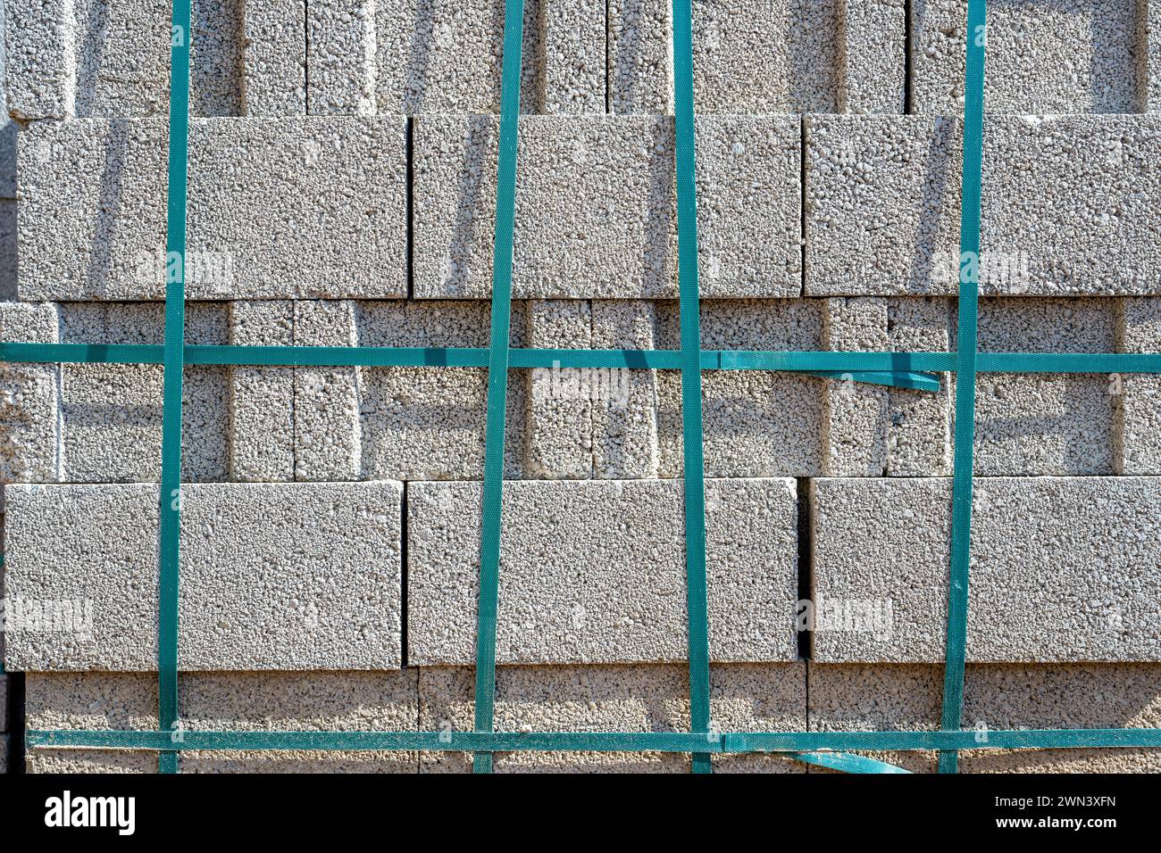 Grauer Zement-Schlackenblock, der übereinander steht und auf der Baustelle mit Streifen gebunden ist Stockfoto