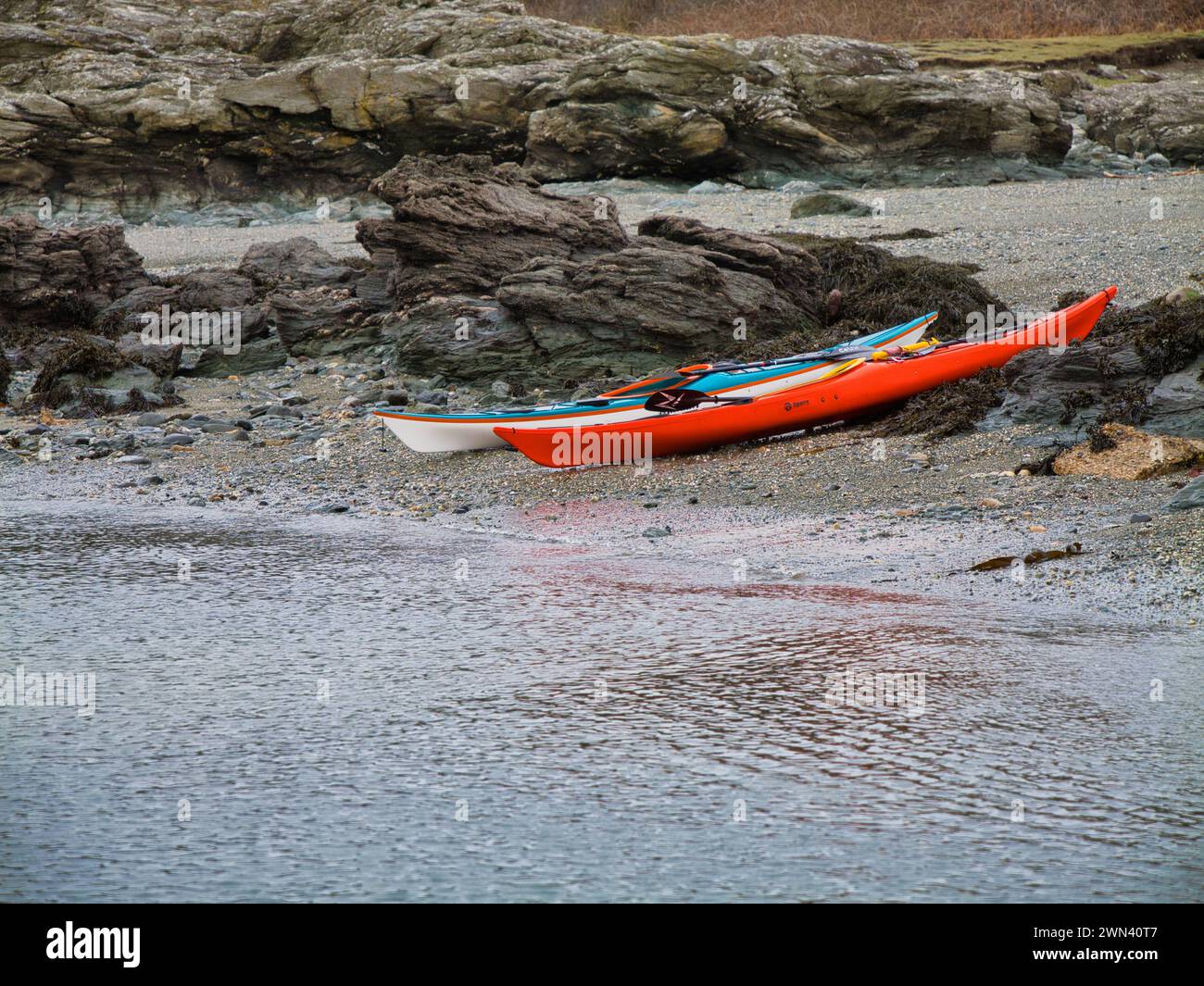 Anglesey, Vereinigtes Königreich - 11. Januar 2024: Zwei Seekajaks an einem einsamen Strand auf der Insel Anglesey in Nordwales, Vereinigtes Königreich. An einem ruhigen, bewölkten Tag im Winter. Stockfoto