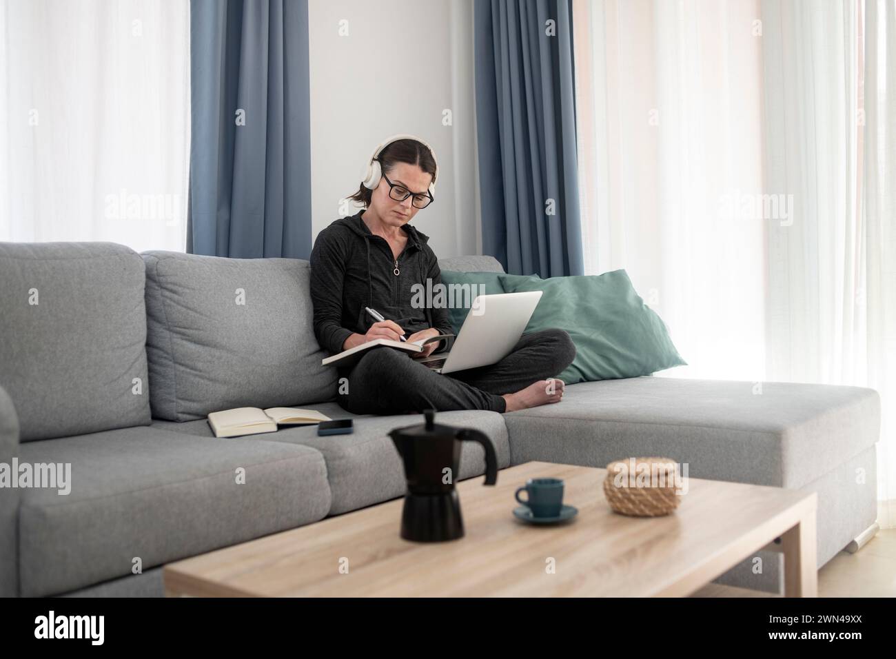 Frau, die auf einer Couch sitzt und von zu Hause aus arbeitet oder studiert, Laptop und Notebook Stockfoto