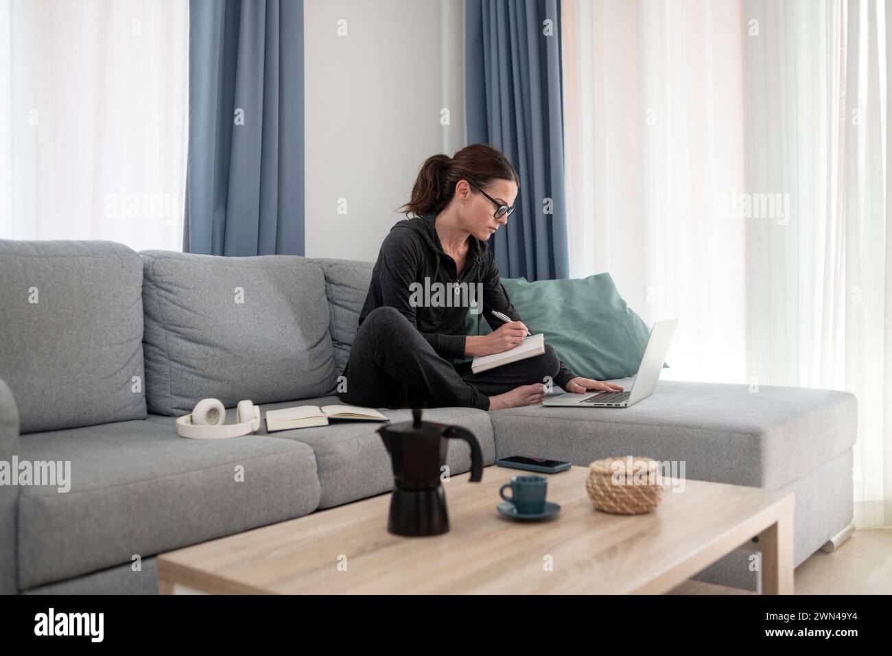 Frau, die auf einer Couch sitzt und von zu Hause aus arbeitet oder studiert, Laptop und Notebook Stockfoto