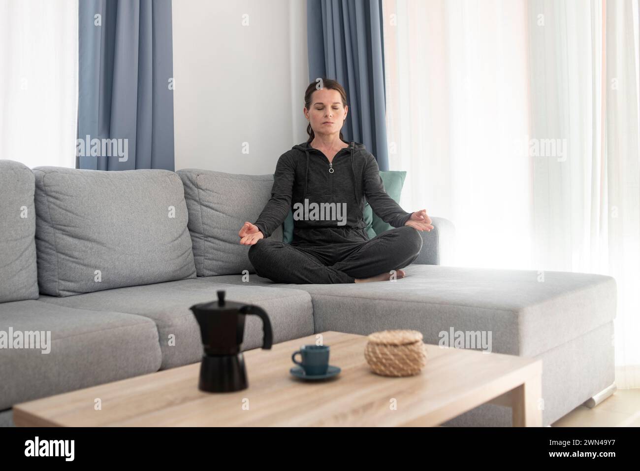 Frau, die auf einer Couch sitzt und mit geschlossenen Augen meditiert. Relaxation, Stressentlastungskonzept. Stockfoto