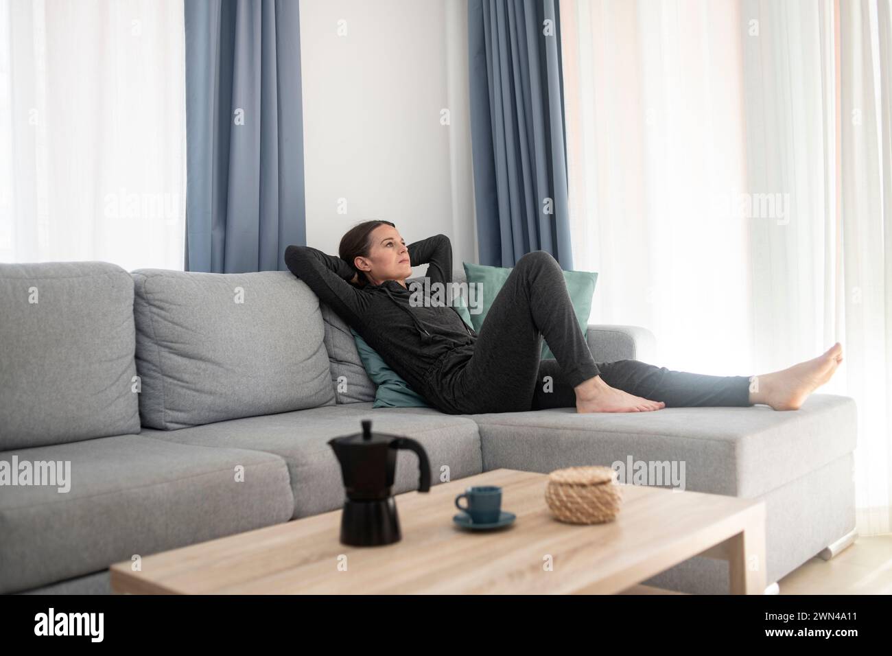 Frau mit den Füßen hoch auf dem Sofa, entspannend zu Hause, Hände hinter dem Kopf. Stockfoto