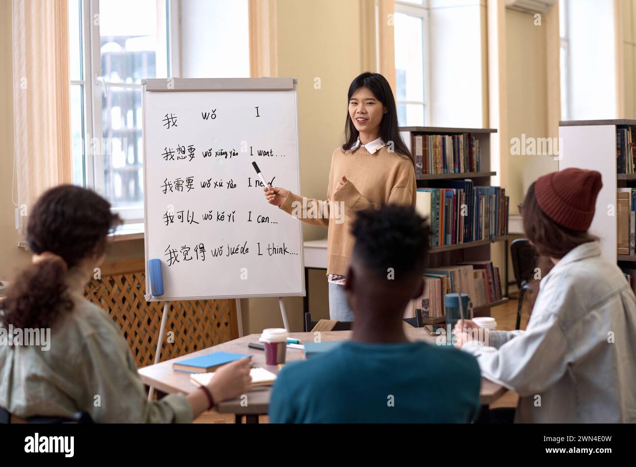 Porträt einer jungen asiatischen Frau, die einer Gruppe von Schülern Chinesisch unterbringt und auf Hieroglyphen auf dem Whiteboard zeigt Stockfoto