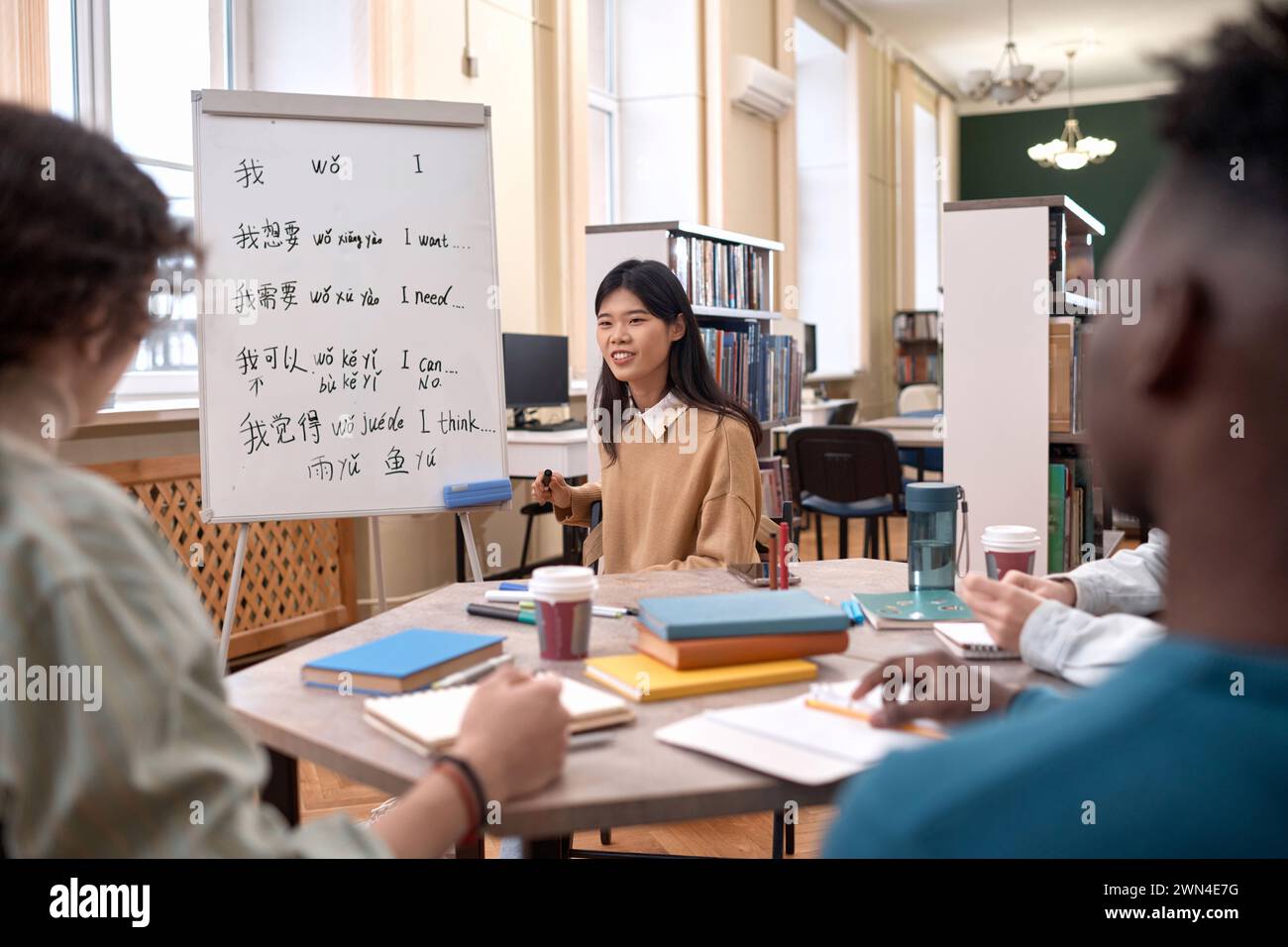 Porträt einer jungen asiatischen Frau als Lehrerin, die mit einer Gruppe von Schülern am Tisch am Whiteboard mit Hieroglyphen-Kopierraum spricht Stockfoto