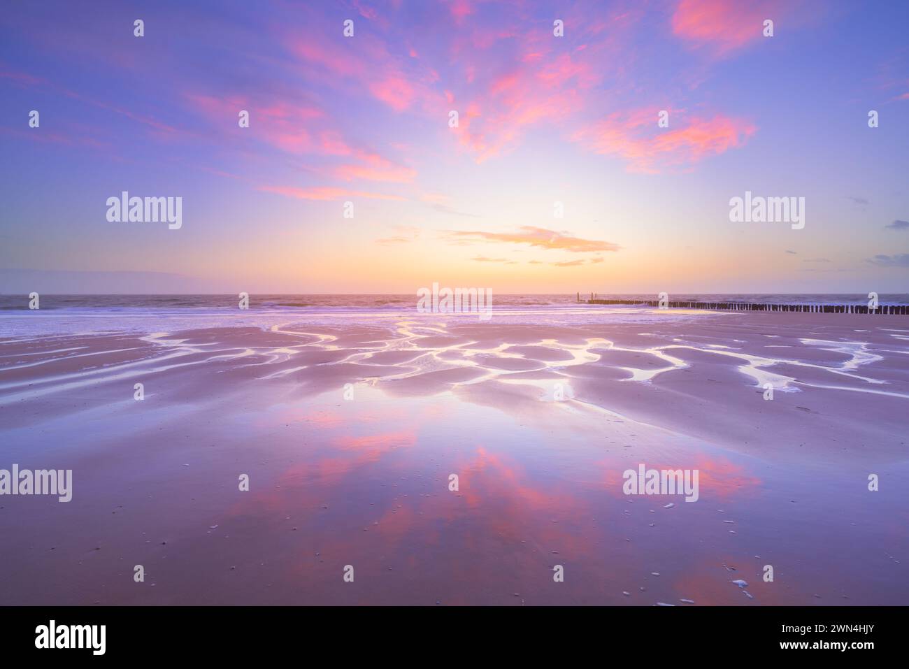 Ein Himmel voller Sonnenuntergang spiegelt sich auf dem nassen Sand des Zoutelande Strandes während eines beruhigenden Sonnenuntergangs an einem ruhigen und schönen Abend, das Wasser fließt. Stockfoto