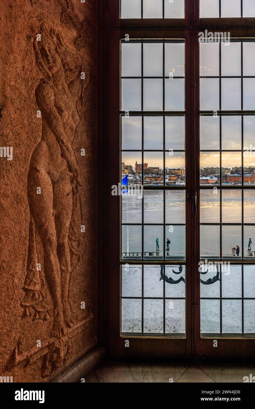 Eine geschnitzte Fensternische in der oberen Galerie des stockholmer Rathauses und Blick durch das Bleifenster auf sodermalm und den gefrorenen malarensee Stockfoto