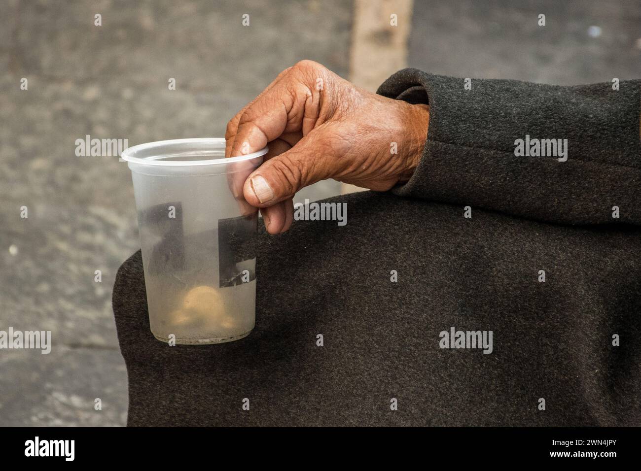 Nahaufnahme eines Mannes Hand, der einen klaren Plastikbecher umschließt und um Geldspenden und finanzielle Hilfe bittet. Stockfoto