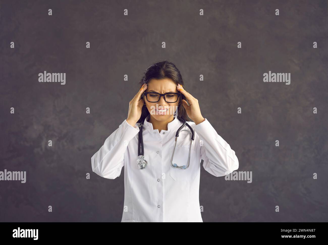 Porträt einer müden Ärztin, die ihre Schläfen massiert und Kopfschmerzen nach einem harten Arbeitstag spürt. Stockfoto