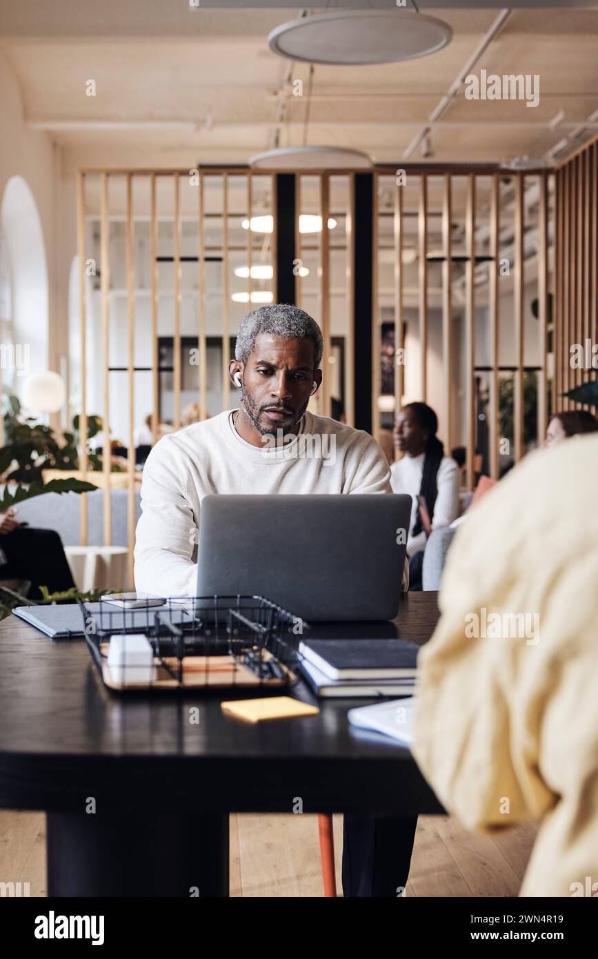 Geschäftsmann, der am Laptop arbeitet, während er im Coworking-Büro am Schreibtisch sitzt Stockfoto