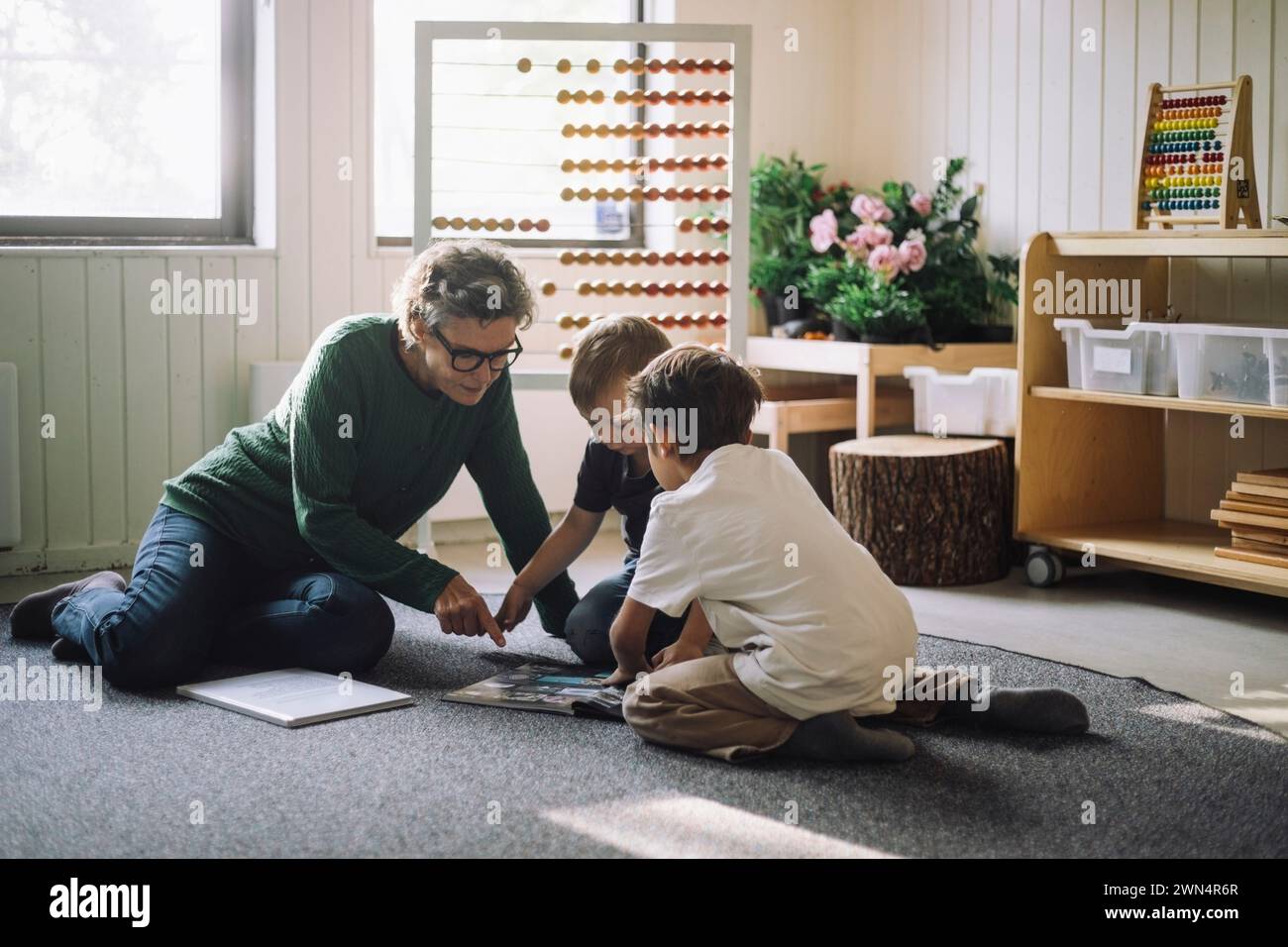 Oberlehrerin sitzt mit Vorschulkindern und liest im Kindergarten Buch Stockfoto