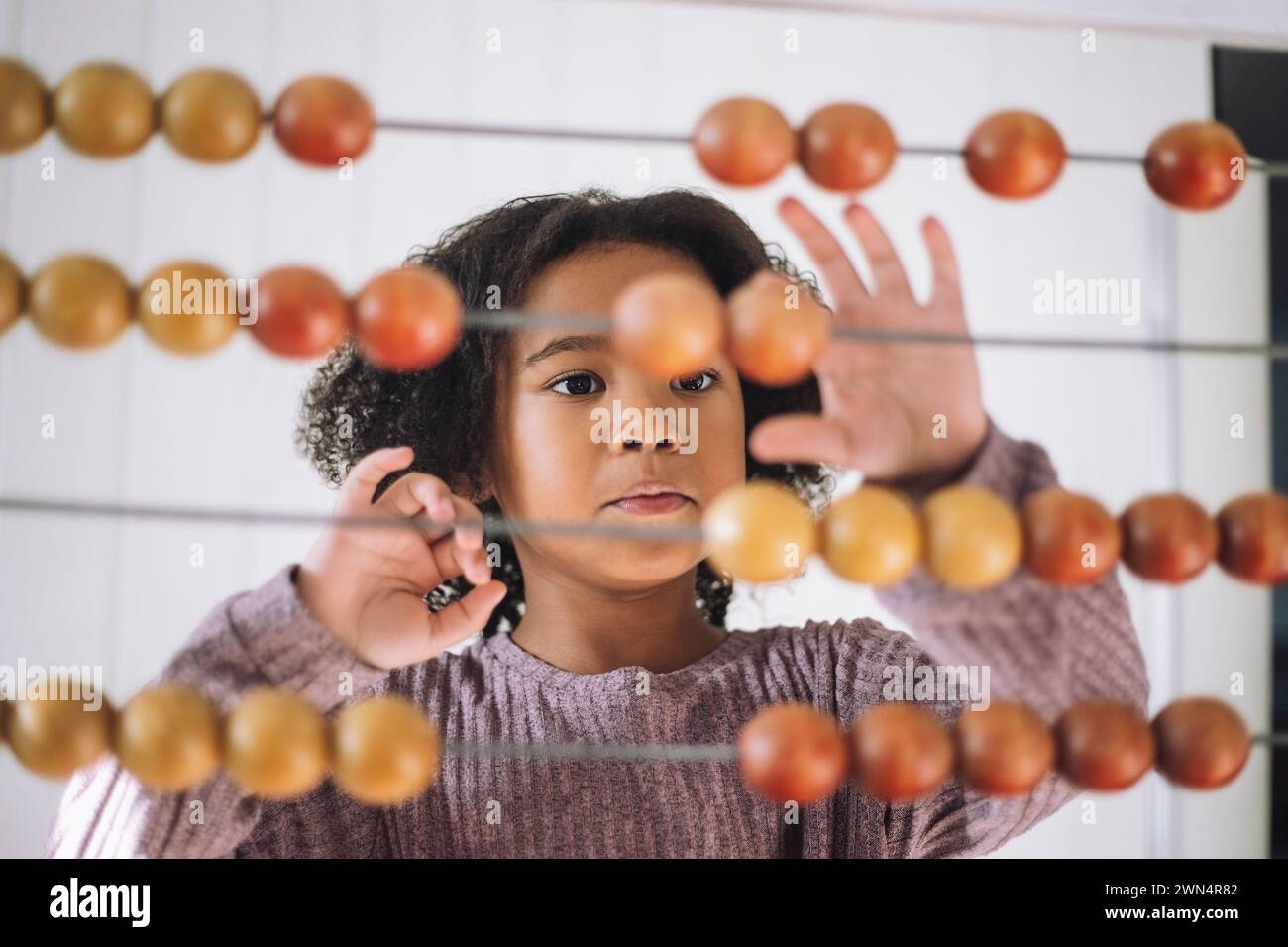Mädchen mit lockigem Haar, das mit Abacus im Kindergarten zählt Stockfoto