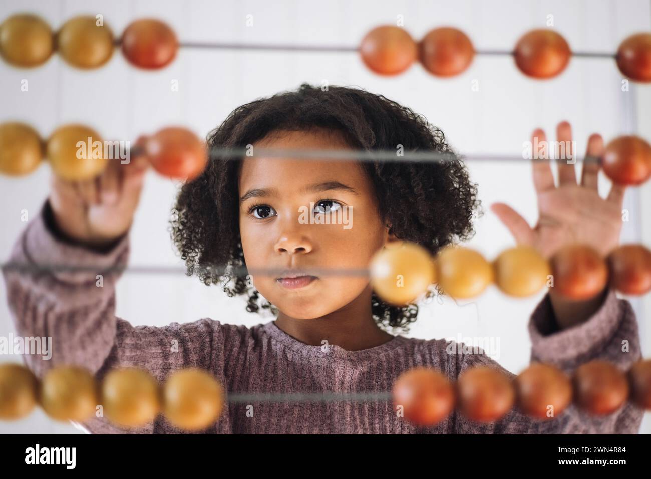 Schulmädchen mit lockigem Haar, das mit Abacus im Kindergarten zählt Stockfoto