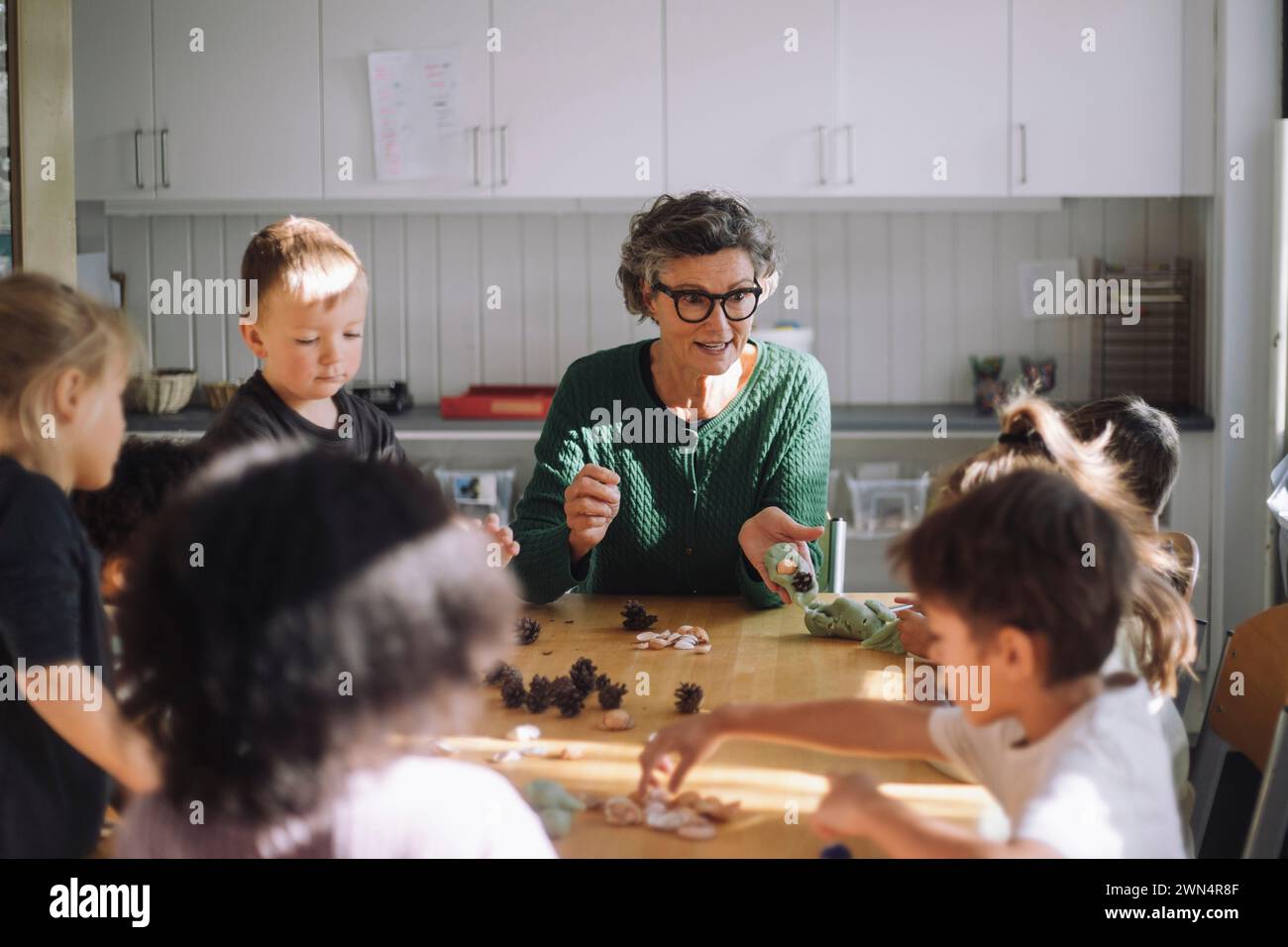 Leitende Lehrerin erklärt den Vorschulkindern, die im Kindergarten im Klassenzimmer sitzen Stockfoto