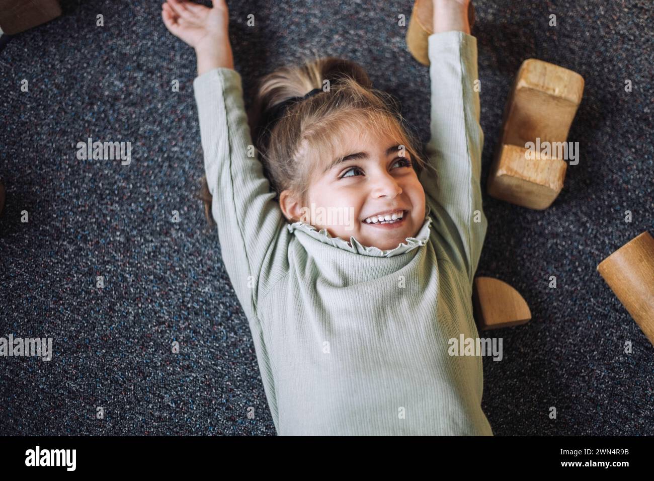 Direkt über dem Blick auf das glückliche Mädchen, das mit erhobenen Armen im Klassenzimmer lag Stockfoto