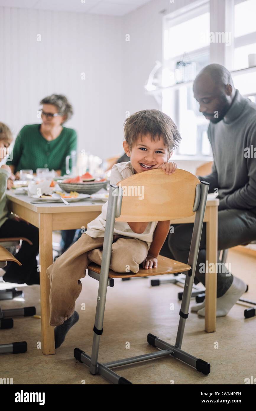 Porträt eines lächelnden Jungen, der während der Mittagspause mit dem Lehrer am Esstisch sitzt Stockfoto
