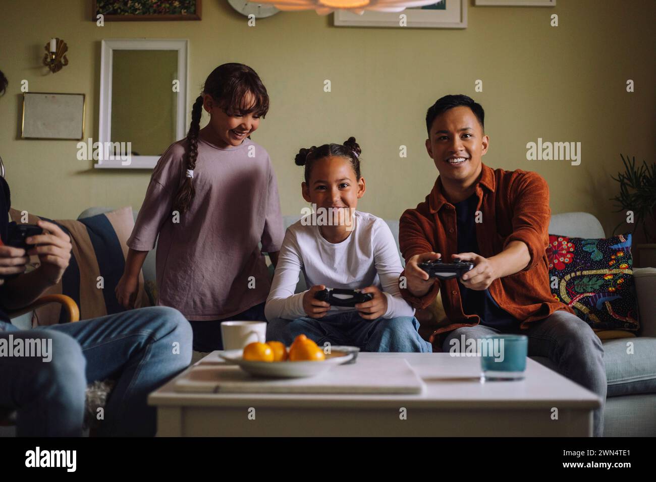 Porträt eines glücklichen Schwulen-Paares, das Videospiel mit der Tochter spielt, während er zu Hause auf dem Sofa sitzt Stockfoto