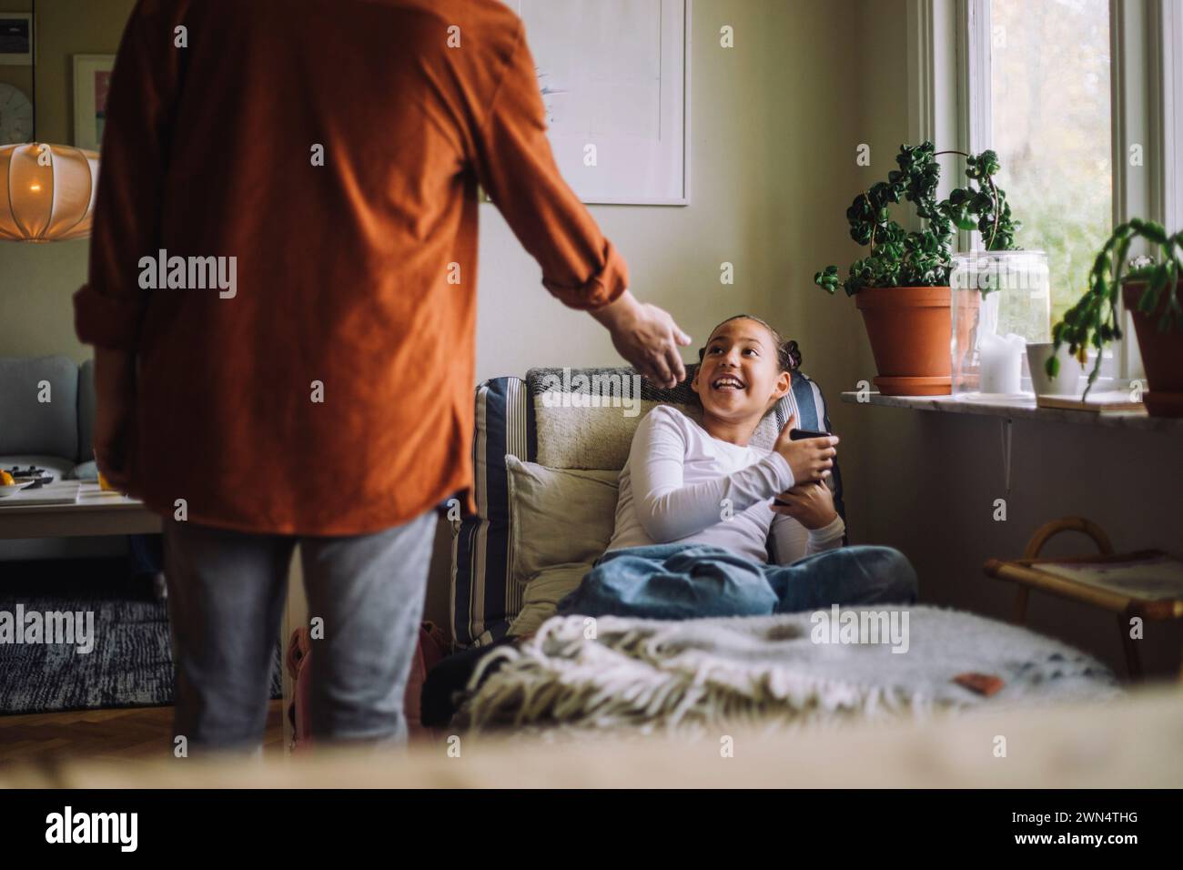 Rückansicht, Mitte des Vaters, der das Smartphone von der Tochter fragt, die zu Hause auf dem Bett sitzt Stockfoto