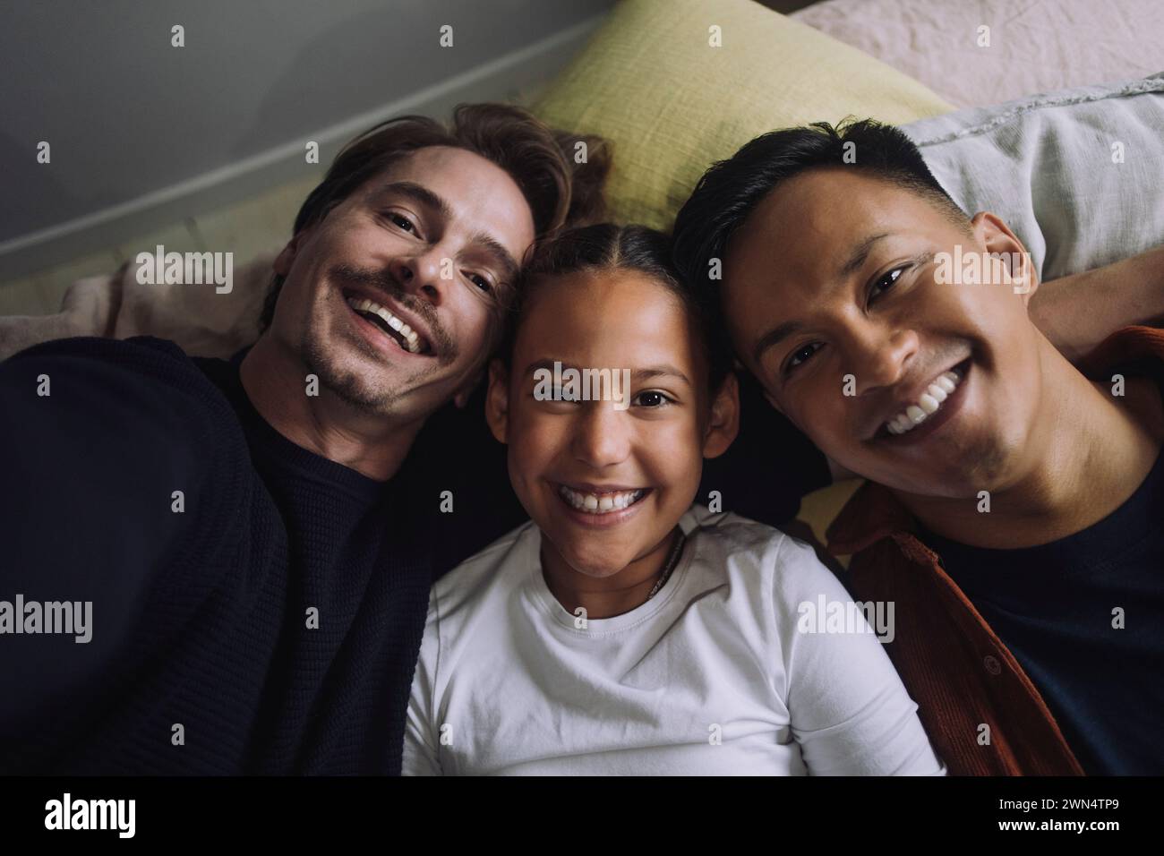 Direkt über dem Porträt eines lächelnden schwulen Paares, das sich mit der Tochter zu Hause liegend Stockfoto