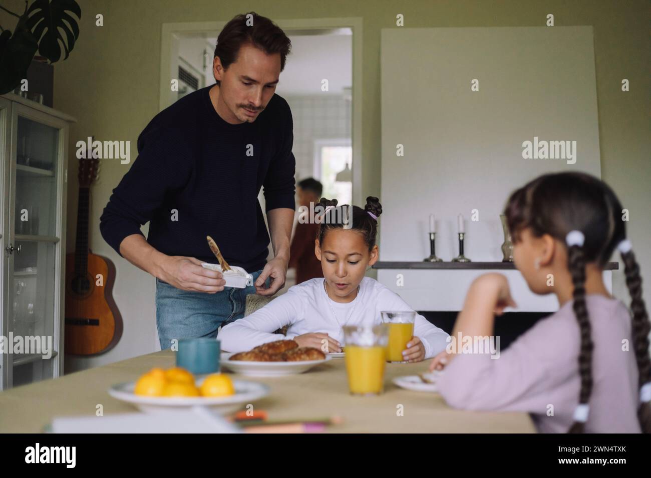 Vater serviert Käseaufstrich für Tochter, die am Esstisch zu Hause frühstückt Stockfoto