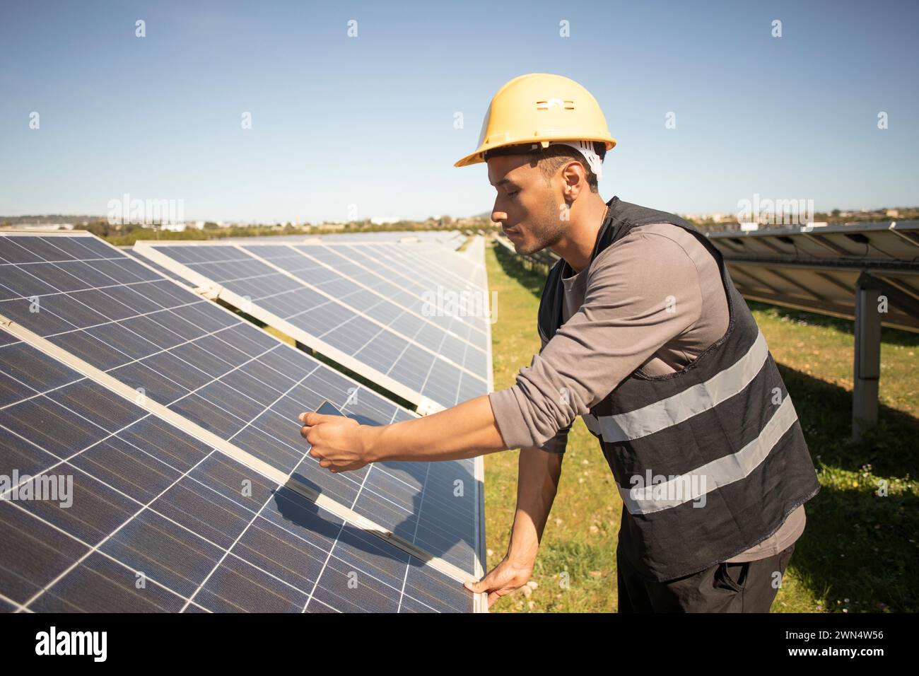 Junger männlicher Ingenieur fotografiert Solarpaneele durch Smartphone im Kraftwerk Stockfoto