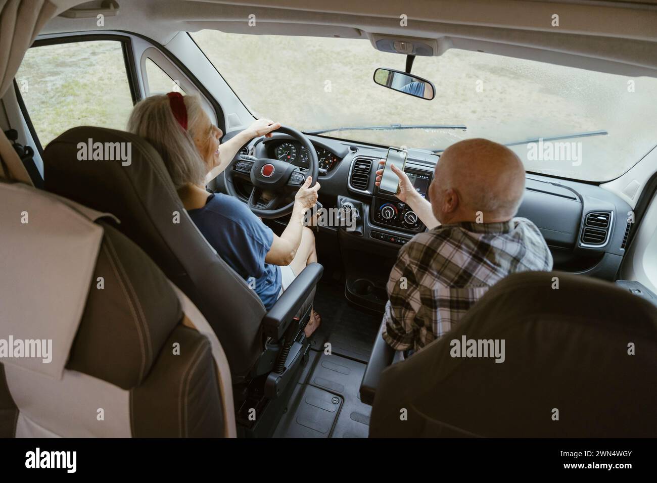 Senior Mann teilt sich das Smartphone mit einer Frau, die während der Fahrt einen Wohnmobil fährt Stockfoto