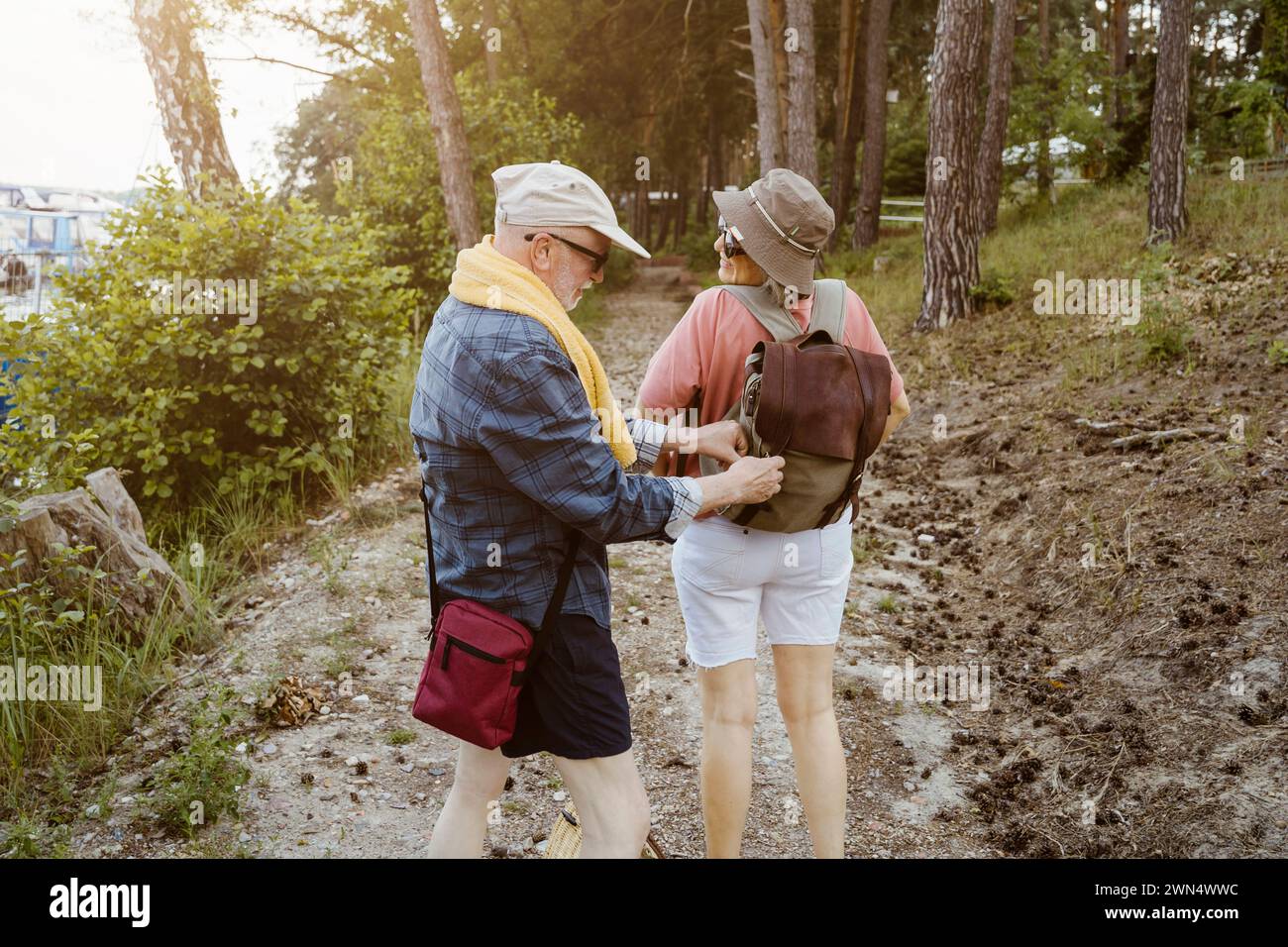 Senior-Mann hilft Frau mit Rucksack beim Wandern im Wald Stockfoto