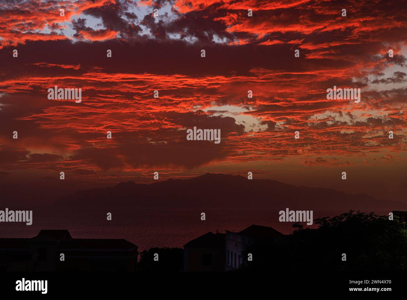 Die Sonne untergeht hinter der Silhouette von ilha brava und beleuchtet die Unterseite von schweren niedrigen Wolken in leuchtendem Rot mit der fogo-Insel im Vordergrund in kap verde Stockfoto