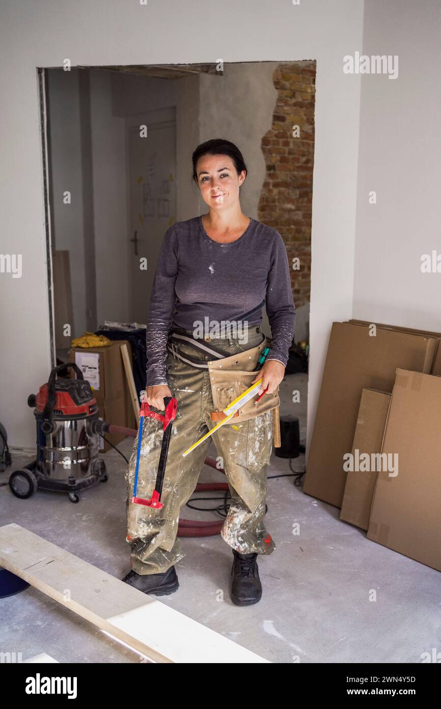 Porträt einer selbstbewussten Zimmerfrau, die Handsäge und Lineal in der Wohnung hält Stockfoto