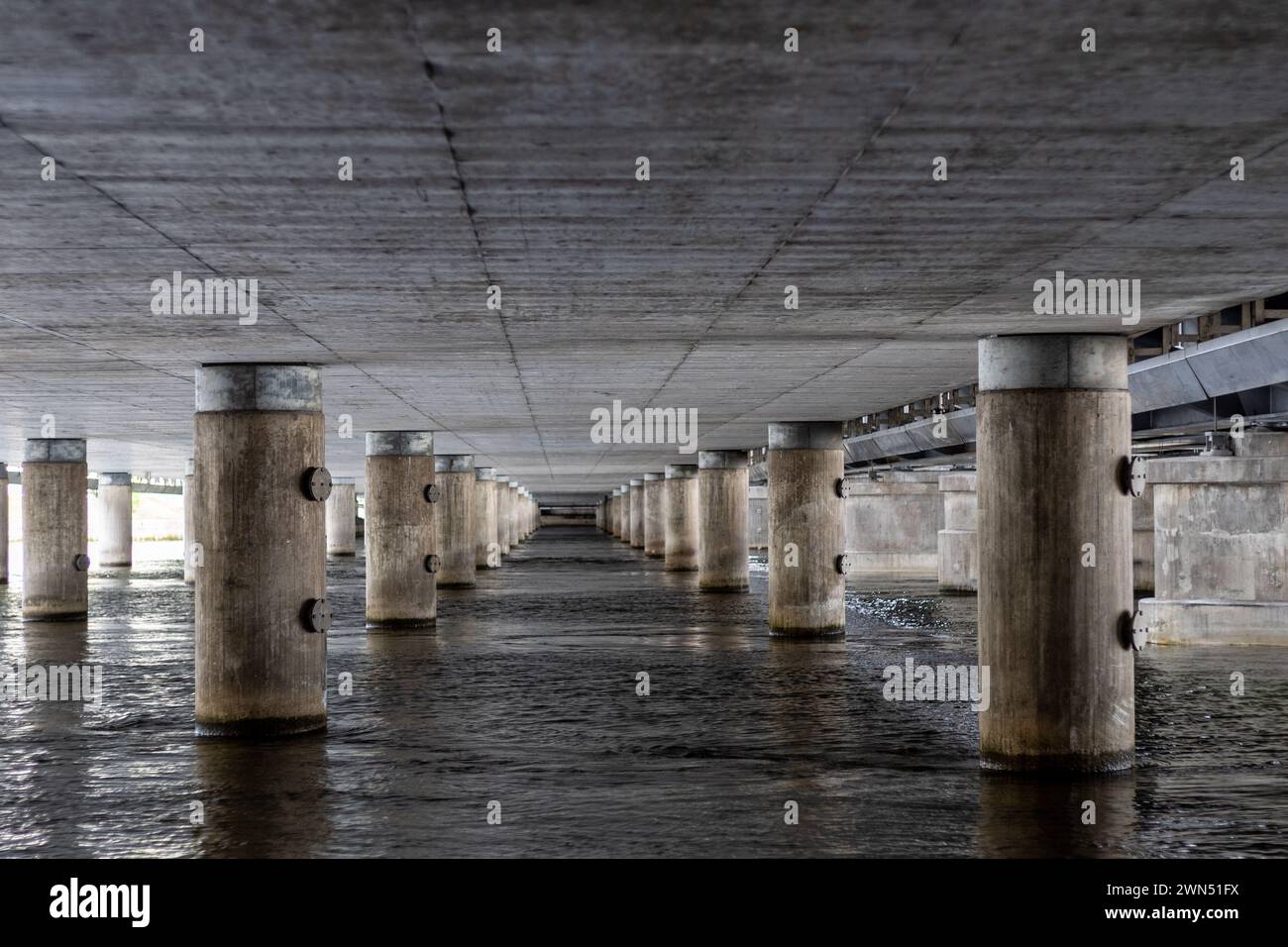 Betonsäulenreihen in strömendem Wasser unter der Brücke. Stockfoto