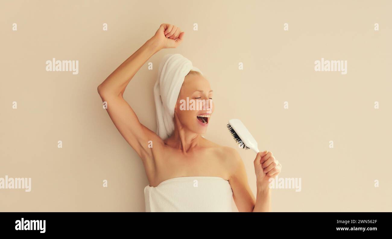 Glückliche fröhliche Frau, die Spaß hat, singt mit Haarkamm und lacht nach der Dusche feuchtes Haar mit Badetuch auf dem Kopf am Morgen zu Hause trocknen Stockfoto