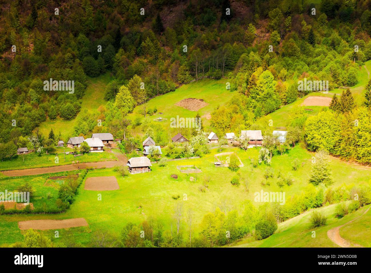 Atemberaubende Aussicht auf eine ländliche Landschaft im Frühling. Dorf zwischen Bäumen und Feldern auf dem grasbewachsenen Hang im verfleckten Licht. Wunderschöne Berglandschaft von tr Stockfoto