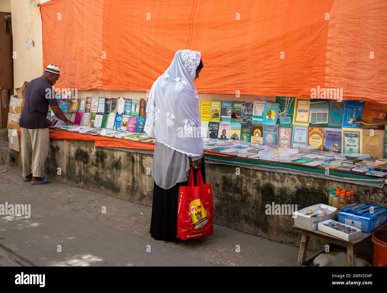 Ein muslimischer Mann und eine muslimische Frau halten an, um sich einen Straßenbuchsstand in Stone Town, Sansibar, Tansania anzuschauen Stockfoto
