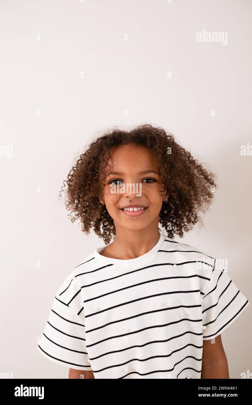 Ein junges Kind mit gemischter Rasse strahlt vor Glück aus und zeigt ein strahlendes Lächeln, das die Unschuld und Freude der Kindheit in einem einfachen, isolierten Umfeld verkörpert Stockfoto