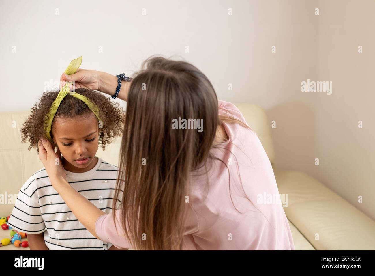 In einem komfortablen Zuhause genießen eine Frau und ihre junge schwarze Tochter eine schöne Zeit, während sie eine spielerische Friseur erleben, die Mutter symbolisiert Stockfoto