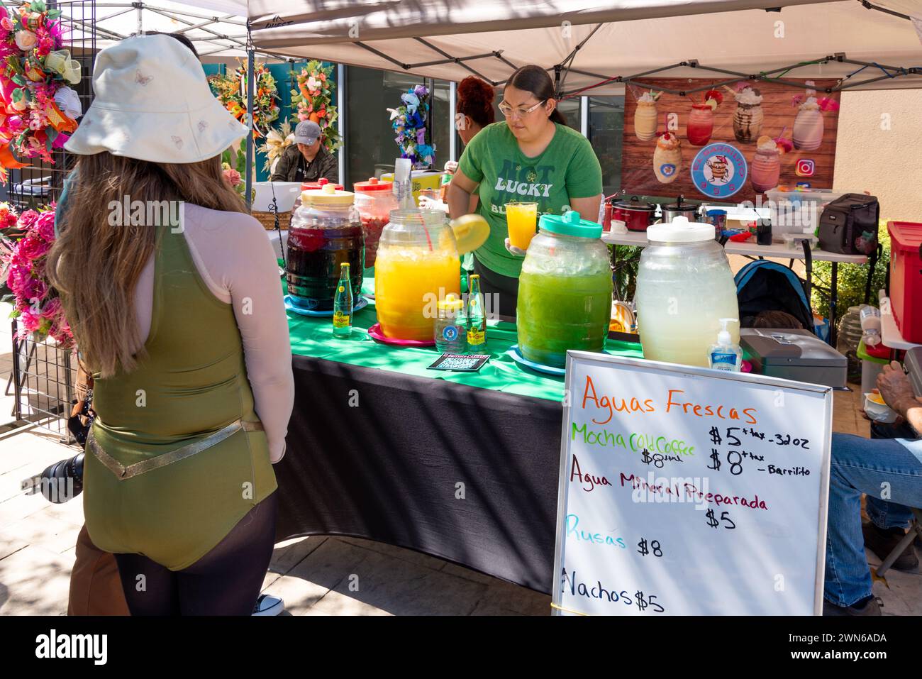 Eine Kundin, eine Frau, an einem Stand mit weiblichen Arbeitern, die bunte Agua-Fresken und frische Getränke beim South Texas Irish fest 2024 in McAllen, Texas, USA servieren. Stockfoto