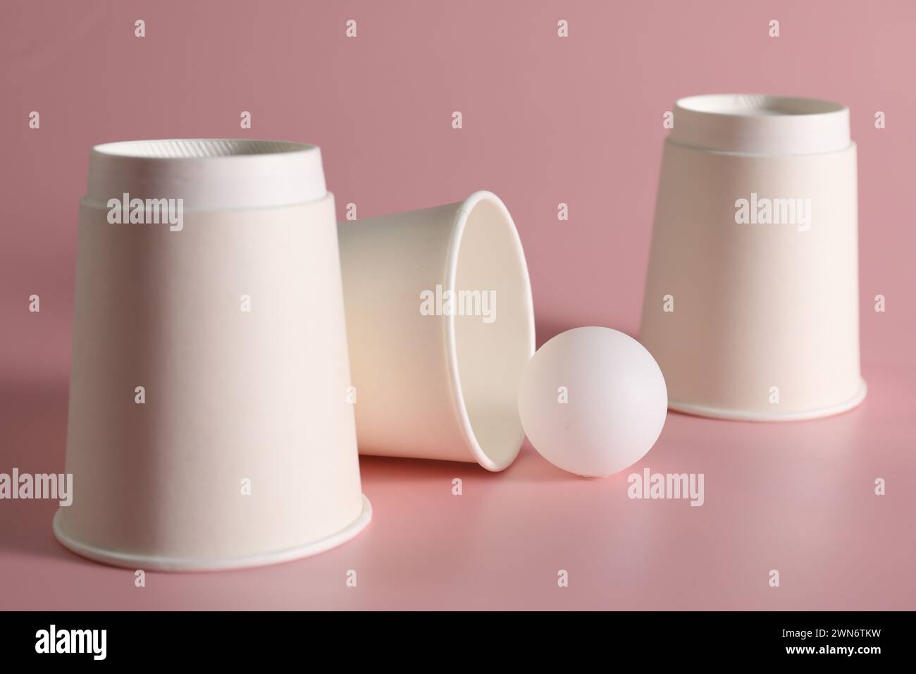 Shell-Spiel. Drei Pappbecher und Ball auf rosa Hintergrund Stockfoto