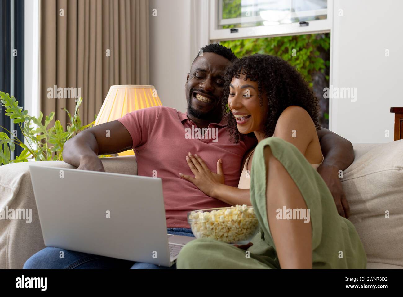 Birassisches afroamerikanisches Paar lacht, während er zu Hause einen Laptop benutzt Stockfoto