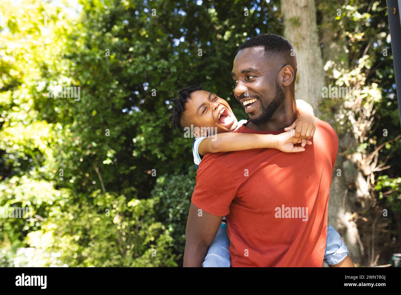 Der afroamerikanische Vater trägt seinen Sohn auf dem Rücken, beide lächeln fröhlich, mit Kopierraum Stockfoto