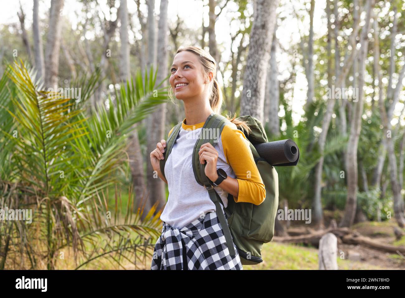 Eine junge Frau mit blonden Haaren lächelt beim Wandern in einem Wald auf einer Wanderung Stockfoto