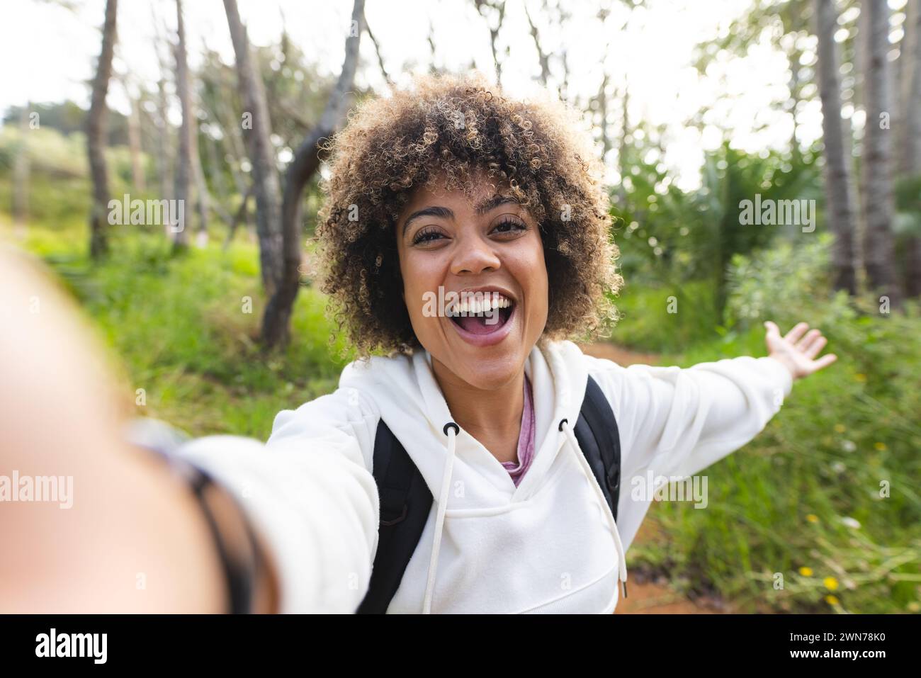 Eine junge birassische Frau mit lockigen Haaren macht ein Selfie, die Arme sind vor Freude auf einer Wanderung ausgestreckt Stockfoto