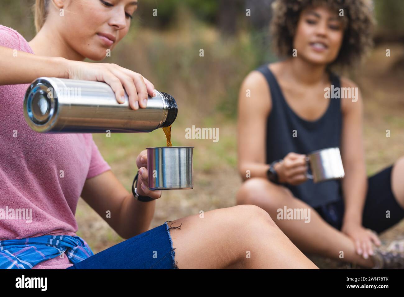 Junge kaukasische Frau gießt einen Drink aus einer Thermoskanne, junge, rassische Frau sieht zu Stockfoto