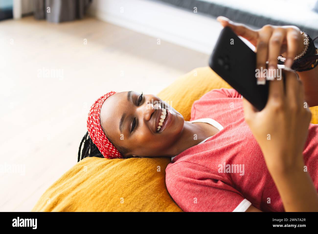 Die junge Afroamerikanerin macht ein Selfie, während sie auf einer gelben Couch liegt Stockfoto