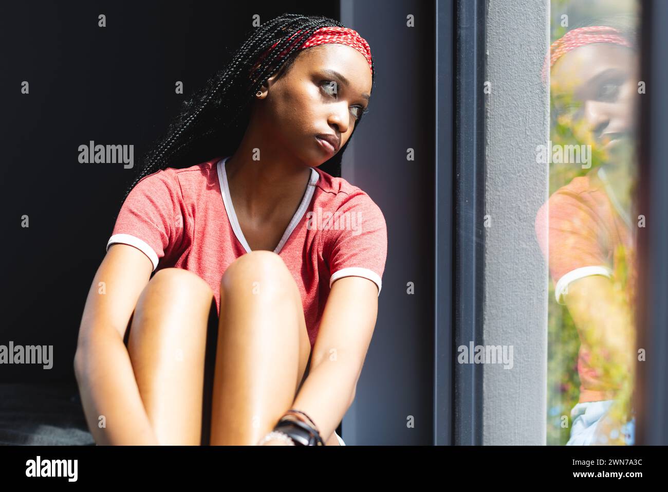 Eine junge Afroamerikanerin schaut aus einem Fenster, tief in Gedanken Stockfoto