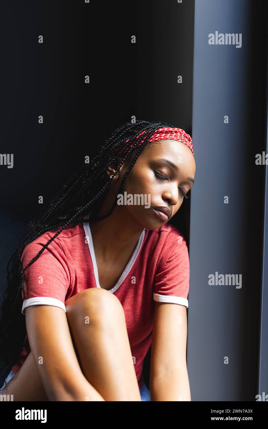 Eine junge Afroamerikanerin sitzt kontemplativ an einem Fenster Stockfoto