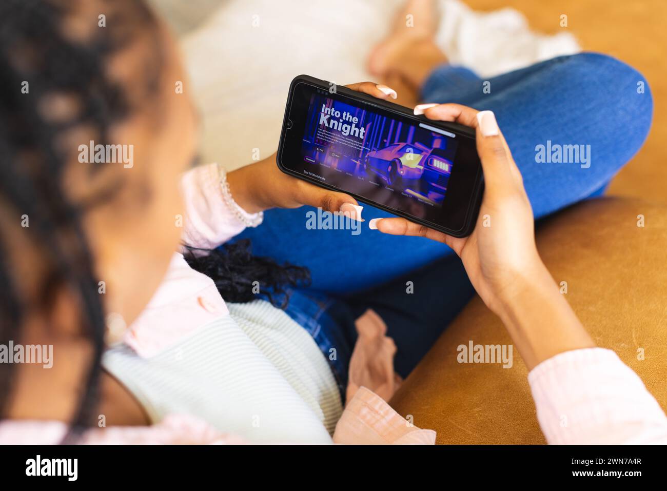 Eine junge Afroamerikanerin nutzt einen Video-Streaming-Dienst auf ihrem Smartphone Stockfoto