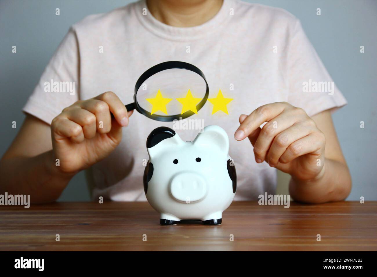 Asiatische Frau, die Lupe in der Hand hält, sieht Schweinebank mit Illustration Stern aus, Sparkonzept Stockfoto
