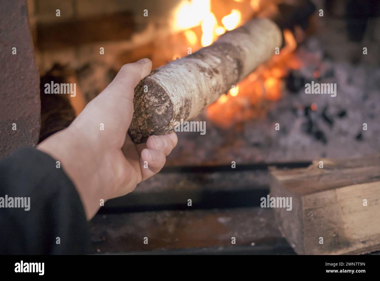 Eine männliche Hand steckt ein Brennholz in einen Ofen, in der Nähe Stockfoto